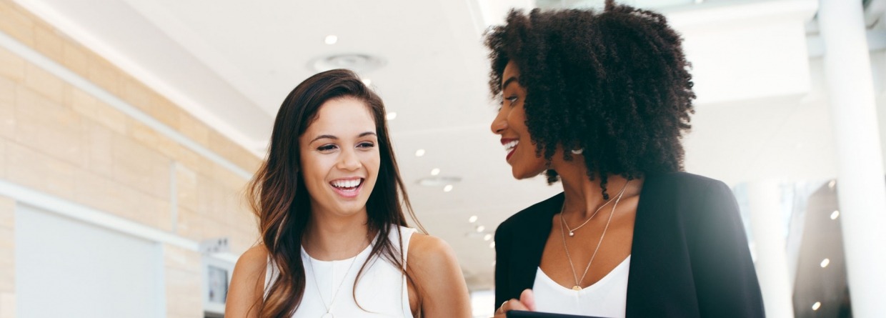 2 blijde jonge vrouwen lopen door het kantoor heen en hebben een overleg