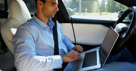 Zakenman met laptop op schoot rijdt in een auto